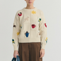 A cream knit sweater with colorful embroidered motifs.