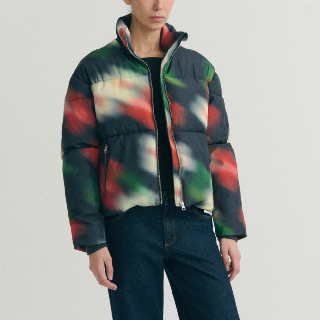A model wearing a colorful abstract-patterned puffer jacket with dark blue jeans.