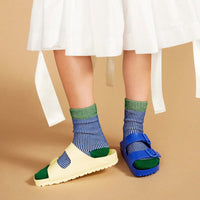 Person wearing a white dress with ruffles and colorful socks on a beige background